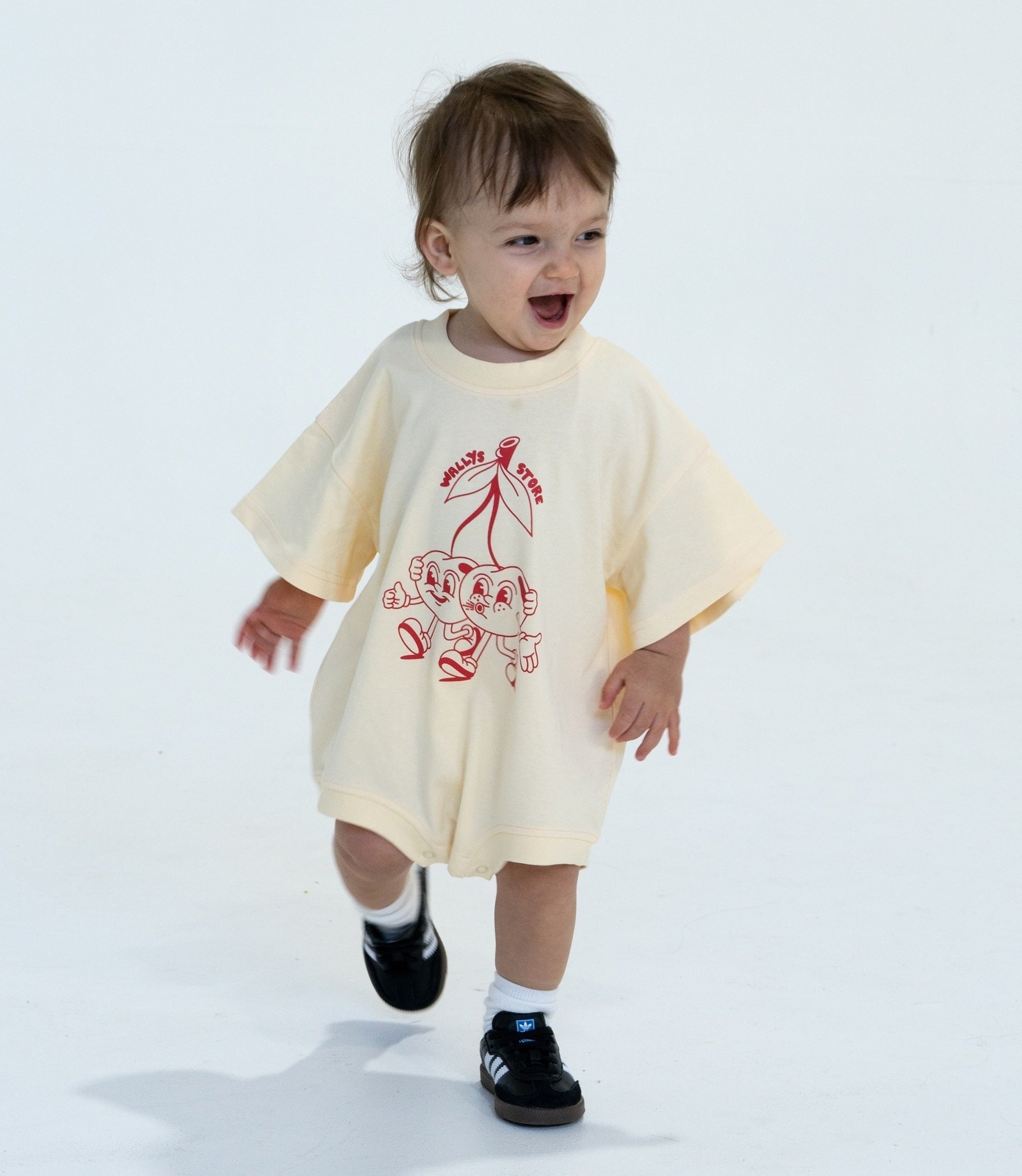 Wally wearing cream childrens romper with cherry artwork in an oversized fit
