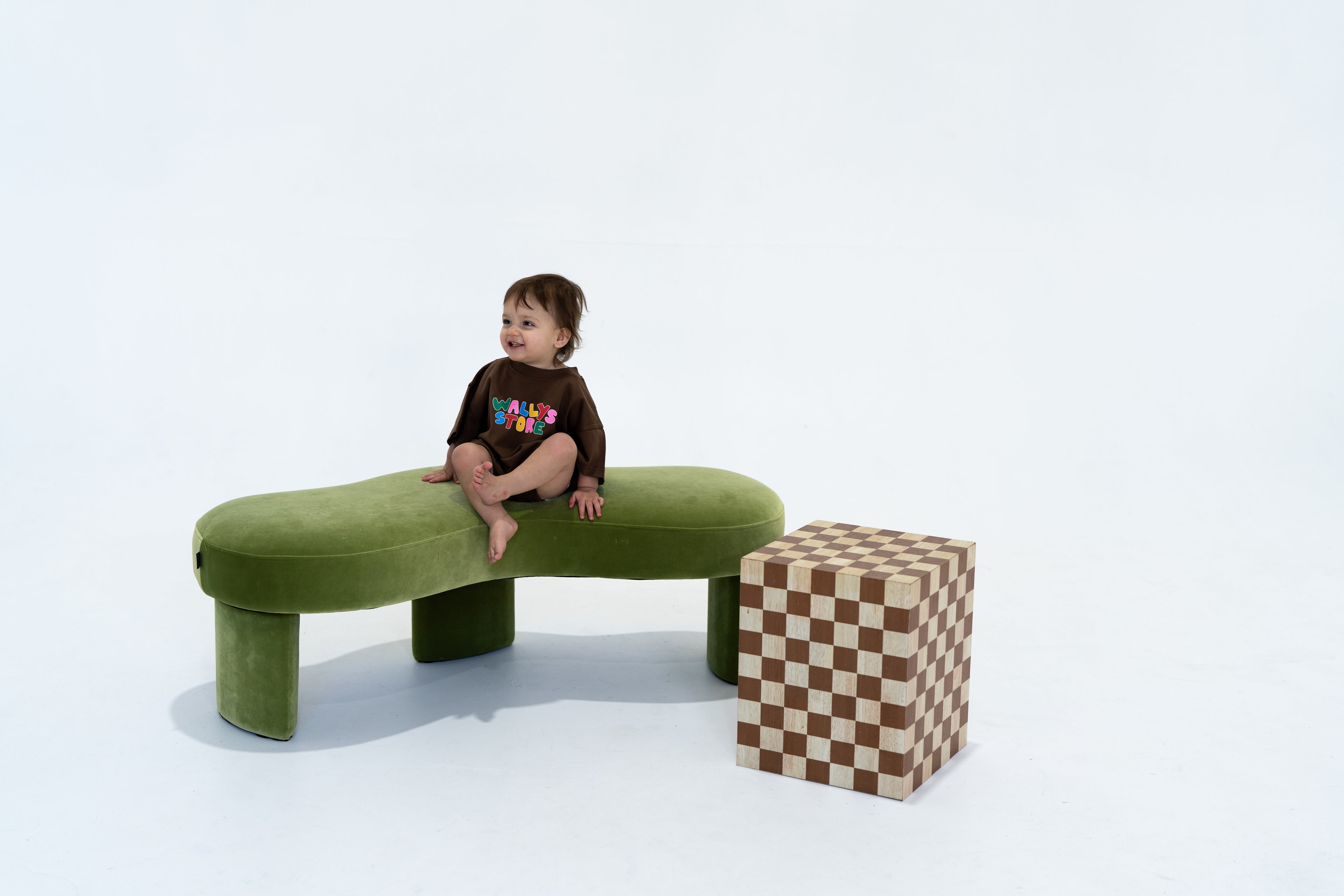 Child sitting on a green bench with a checkered box next to it on a white background